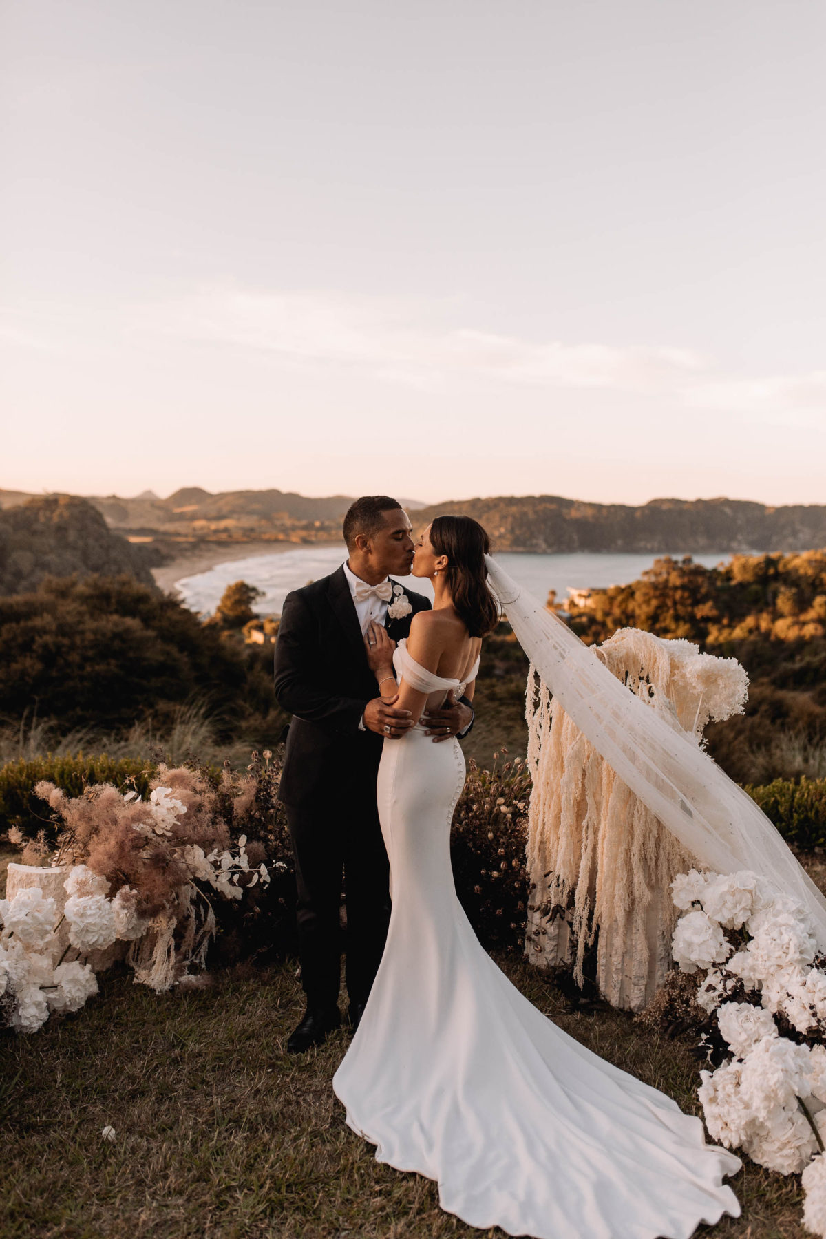 Bride and groom kiss on the cliffs in New Zealand - the perfect destination wedding location